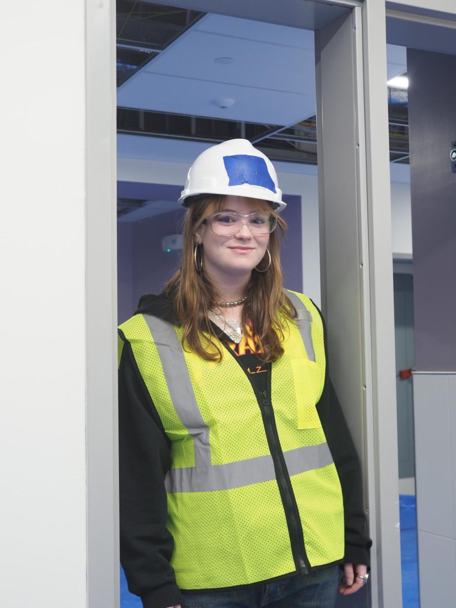 Miranda Brown ‘27 standing in the open space beside a classroom door where an interior window will be installed.